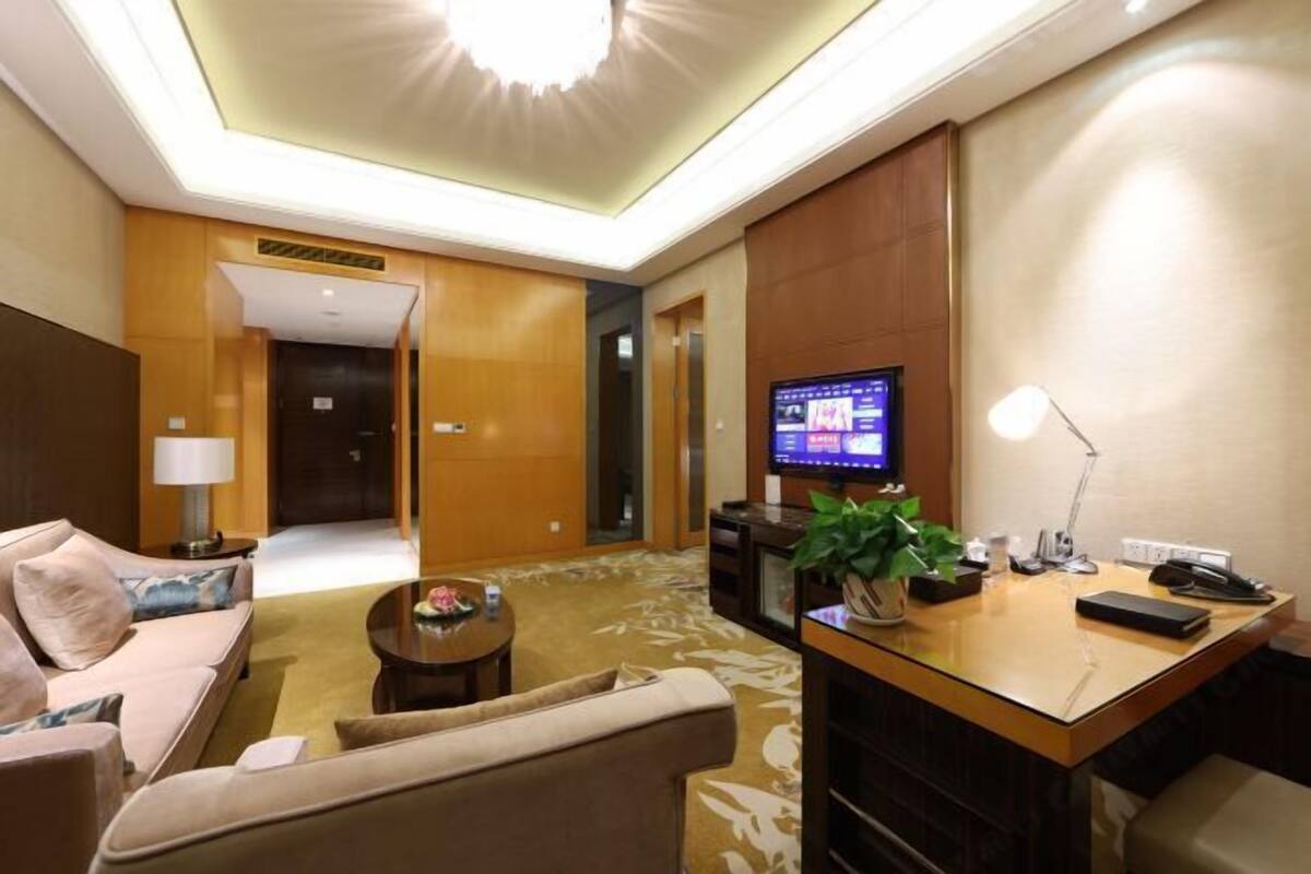 A hotel lobby with a sofa, a small table, a desk with a computer, a TV, and a plant.