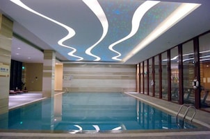 Una piscina interior con diseño moderno, que incluye una lámpara de techo ondulada y una barrera de vidrio transparente.