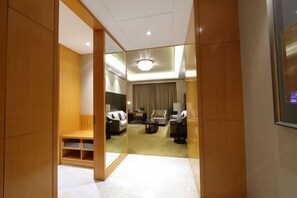 Habitación de hotel con armario de madera, zona de estar con sofá y sillones, una mesita y una lámpara de techo.
