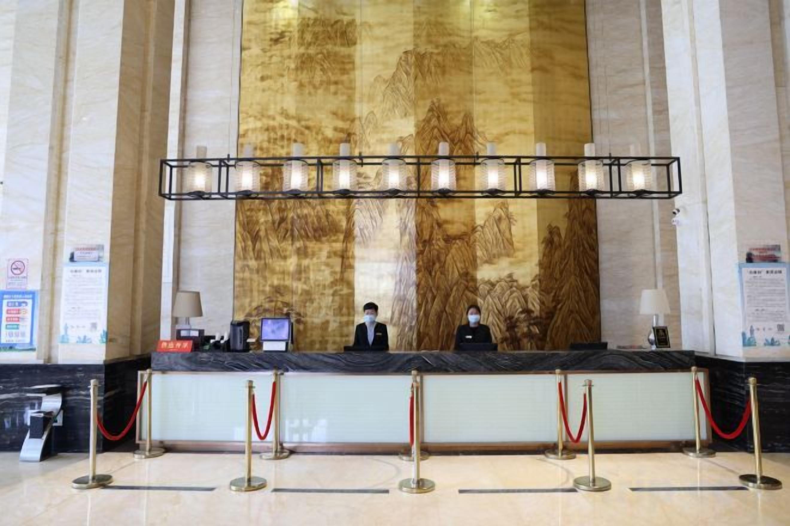 A reception desk with two staff members, a large wall mural, and a chandelier.