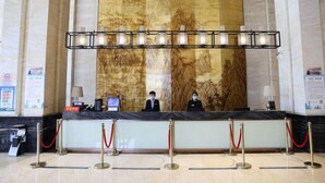 A reception desk with a marble counter, two receptionists, a large wall mural, and a row of red ropes and stanchions. - Huifeng Hotel (Shuyang)