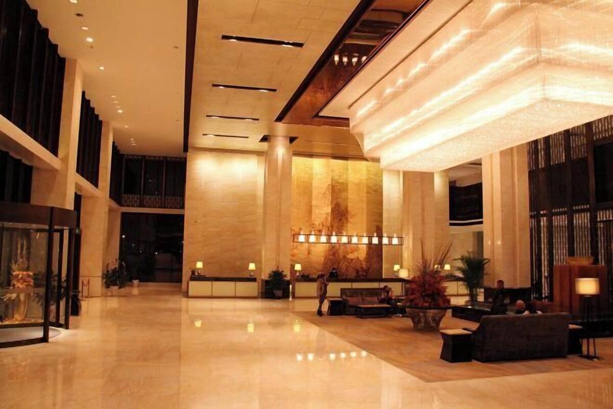 A spacious lobby with a high ceiling, a reception desk, seating area, and a large chandelier.