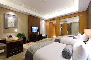Habitación de hotel con dos camas, un escritorio con computadora, televisión y un espejo grande.
