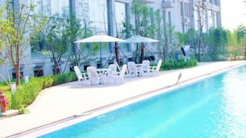 A swimming pool with lounge chairs and umbrellas, surrounded by a building with large windows.