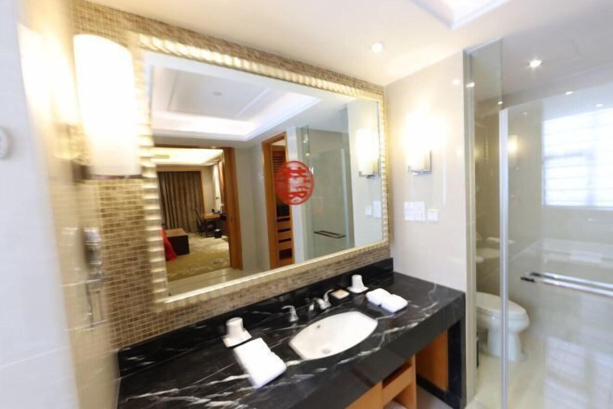 Un baño moderno con un espejo grande, encimera de mármol negro y cabina de ducha de vidrio.