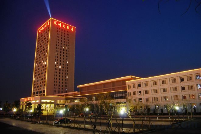 A multi-story hotel with a prominent tower, a covered walkway, and a parking area.