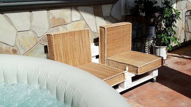 A hot tub with wicker lounge chairs and a stone wall backdrop. - Cilento Loft (Ascea)