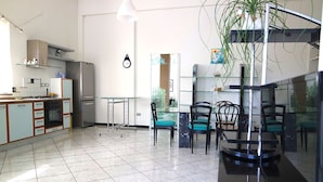 A modern kitchen with a refrigerator, stove, and cabinets. There is a dining area with chairs and a table. - Cilento Loft (Ascea)