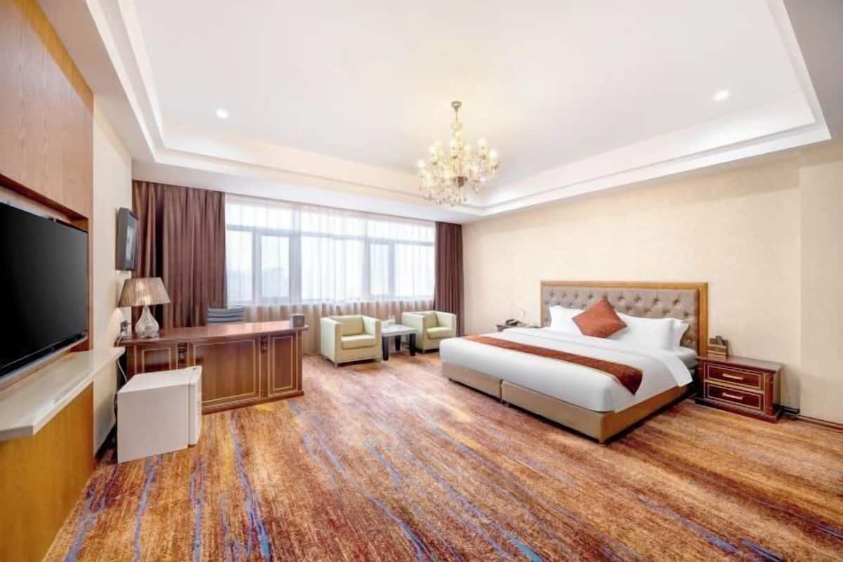 A hotel room with a large bed, a desk, a TV, and a chandelier.