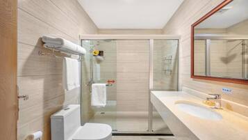 Une salle de bain moderne avec une douche à parois de verre, des toilettes blanches et un lavabo beige avec un miroir au-dessus.