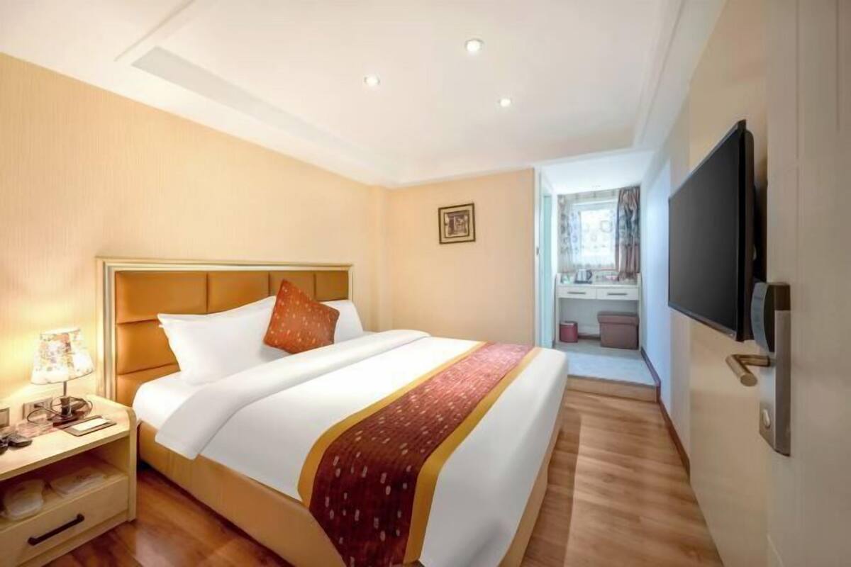 A hotel room with a bed, bedside table, lamp, and a television mounted on the wall.
