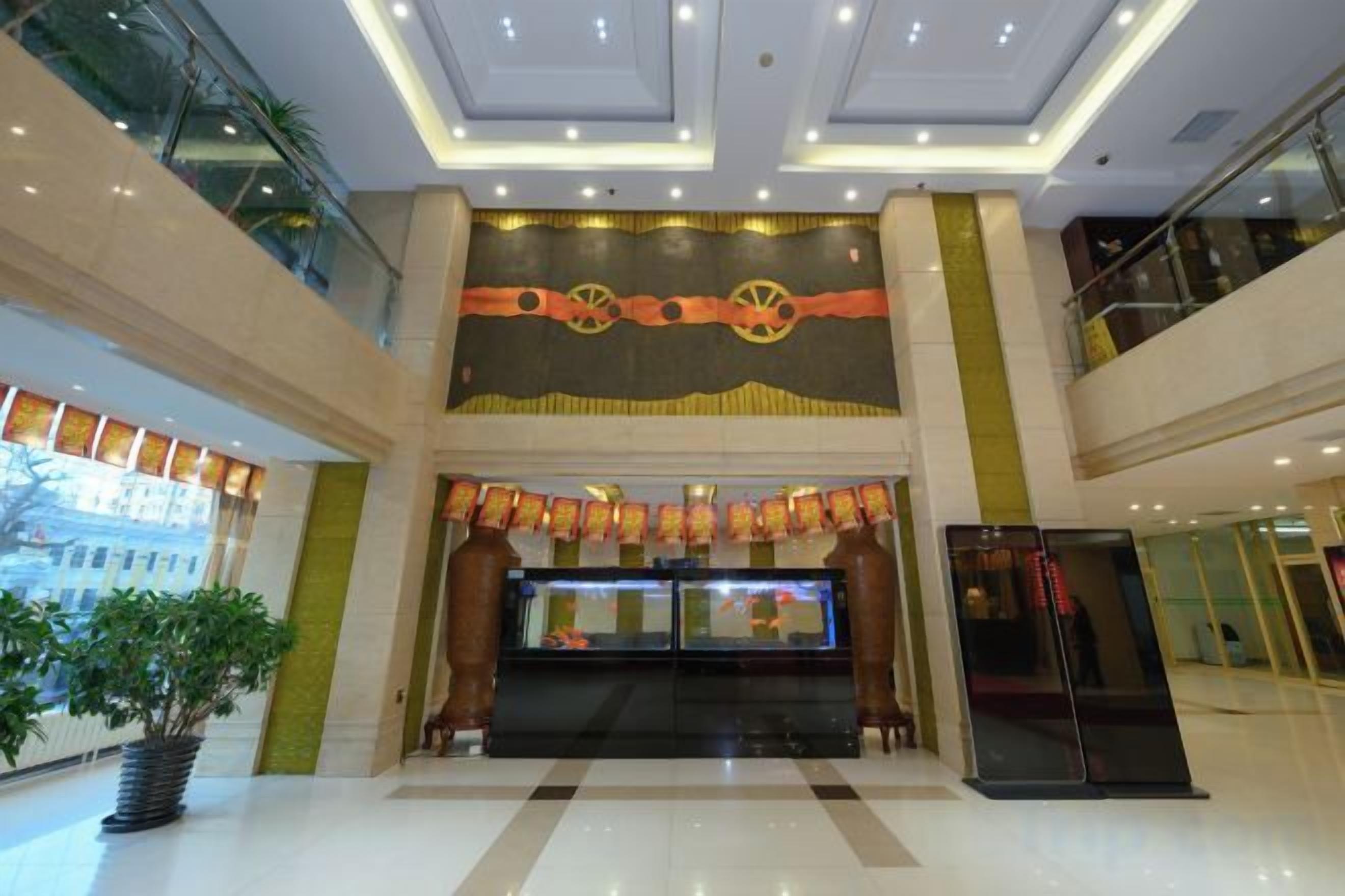 A hotel lobby with a reception desk, a large digital display, and a potted plant.