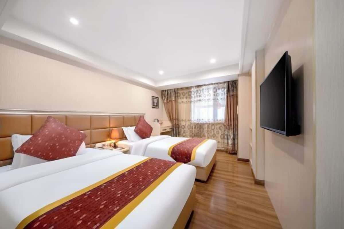 A hotel room with two beds, a TV, and a window with curtains.