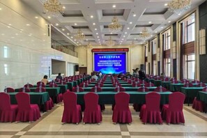 Un salón de conferencias con mesas y sillas dispuestas en filas, una pantalla grande al frente y candelabros.