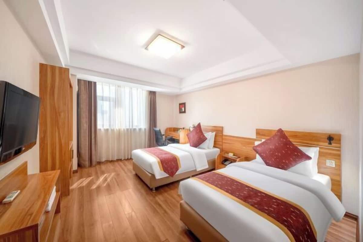 A hotel room with two beds, a TV, a desk, and a window with curtains.