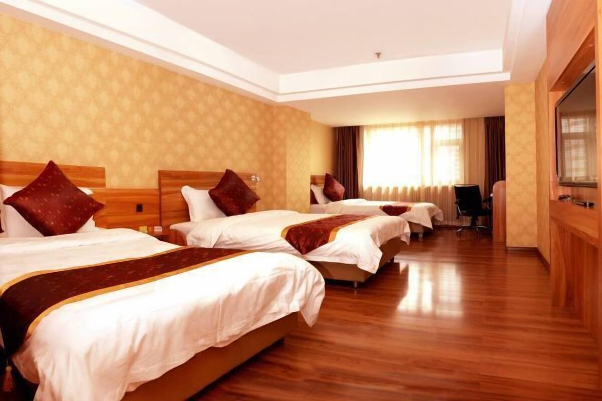 A hotel room with three beds, wooden flooring, and a large window with curtains.
