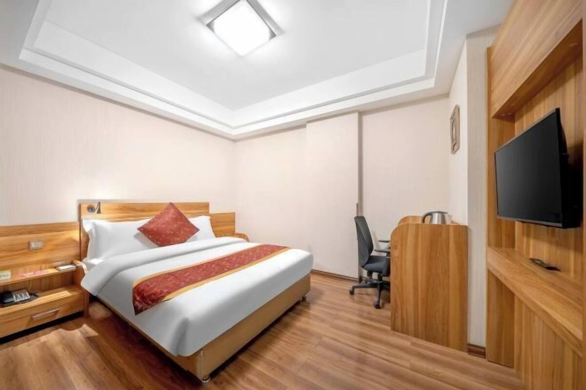 A hotel room with a bed, a desk, a chair, a TV, and a wooden wardrobe.