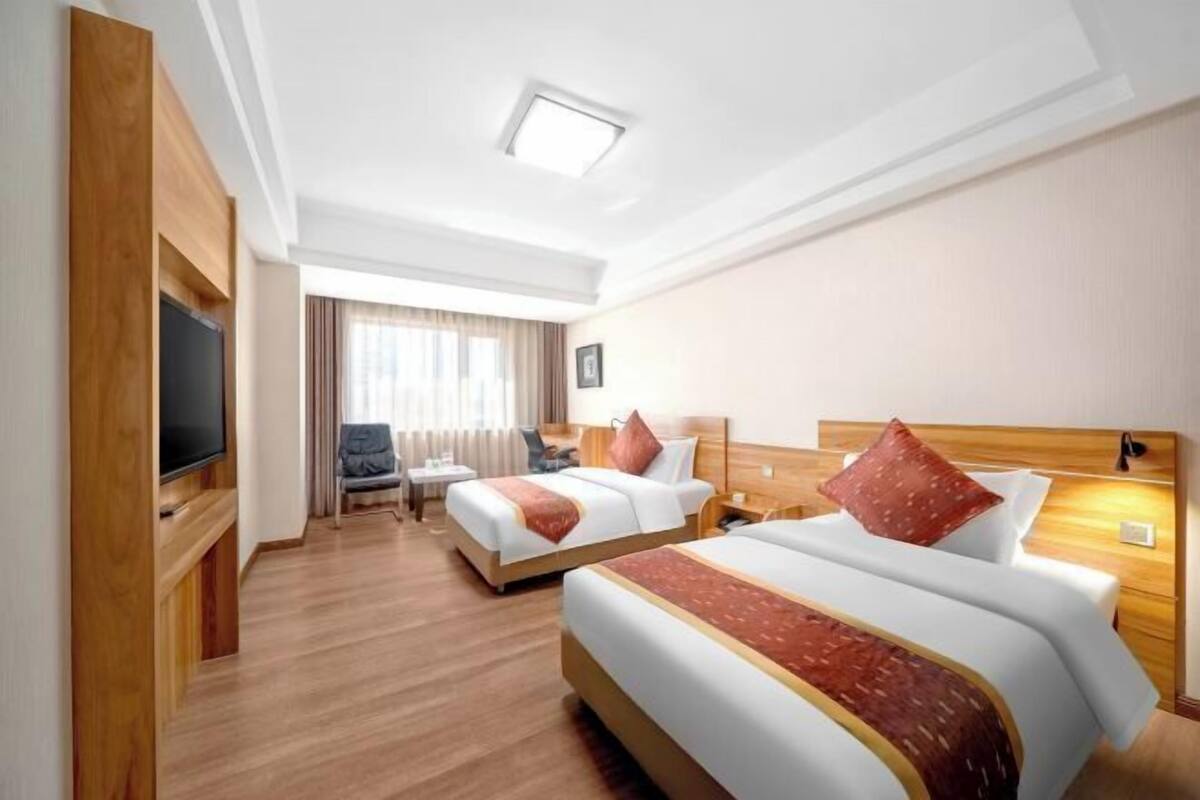 A hotel room with two beds, a TV, a desk, and a chair.