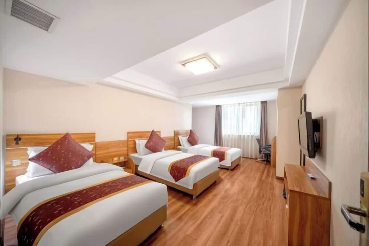 A hotel room with three beds, wooden flooring, a flat-screen TV, and a desk.