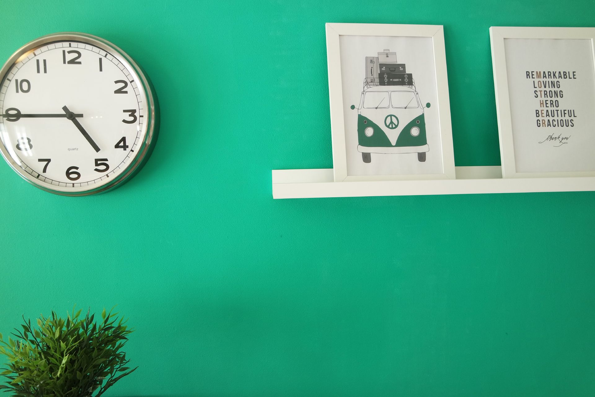 A wall clock, a framed illustration of a van, and a framed inspirational quote on a green wall.