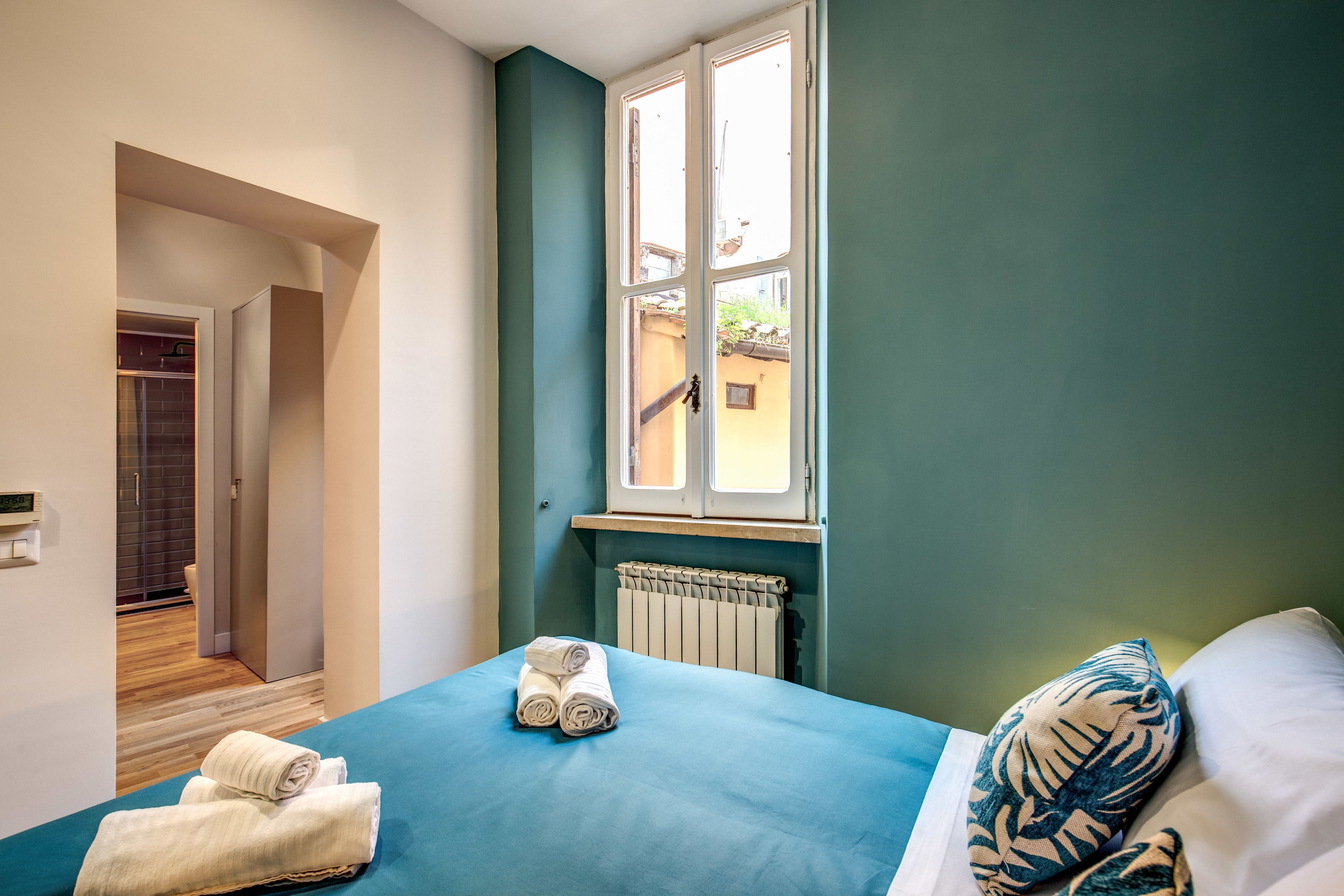Une chambre avec une couvre-lit bleue, deux serviettes enroulées, une fenêtre donnant sur un beau paysage et un radiateur.