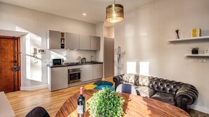 Une cuisine moderne avec des meubles blancs, un four à micro-ondes et une cuisinière. On y trouve également un coin repas avec une table en bois, une bouteille de vin et une plante verte.