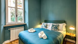 Une chambre à coucher avec un grand lit, une fenêtre, un radiateur et une table de chevet avec une lampe.