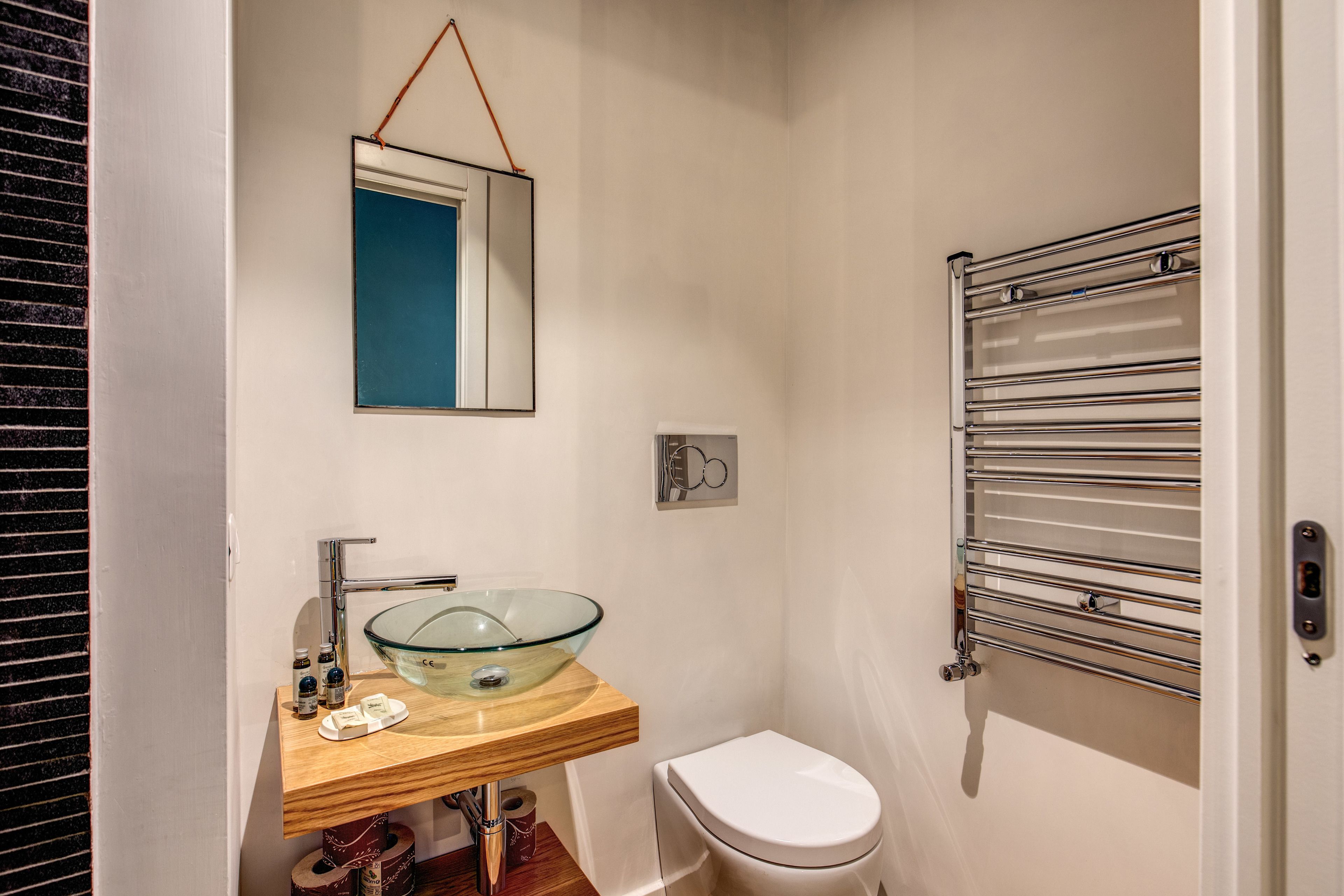 A bathroom with a glass bowl sink, a white toilet, a towel rack, and a mirror.