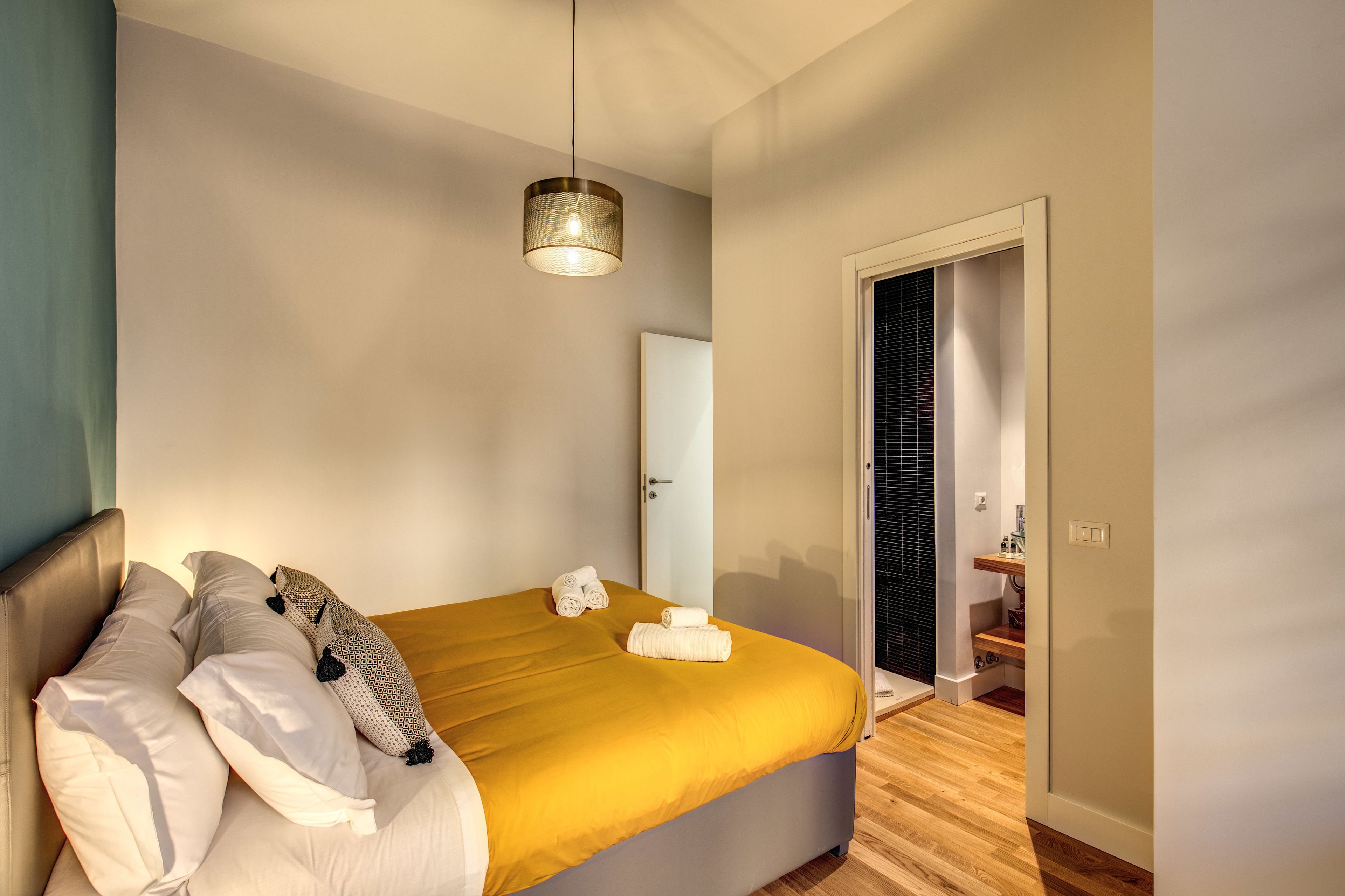 A modern bedroom with a bed, pillows, a yellow blanket, and a hanging light fixture.