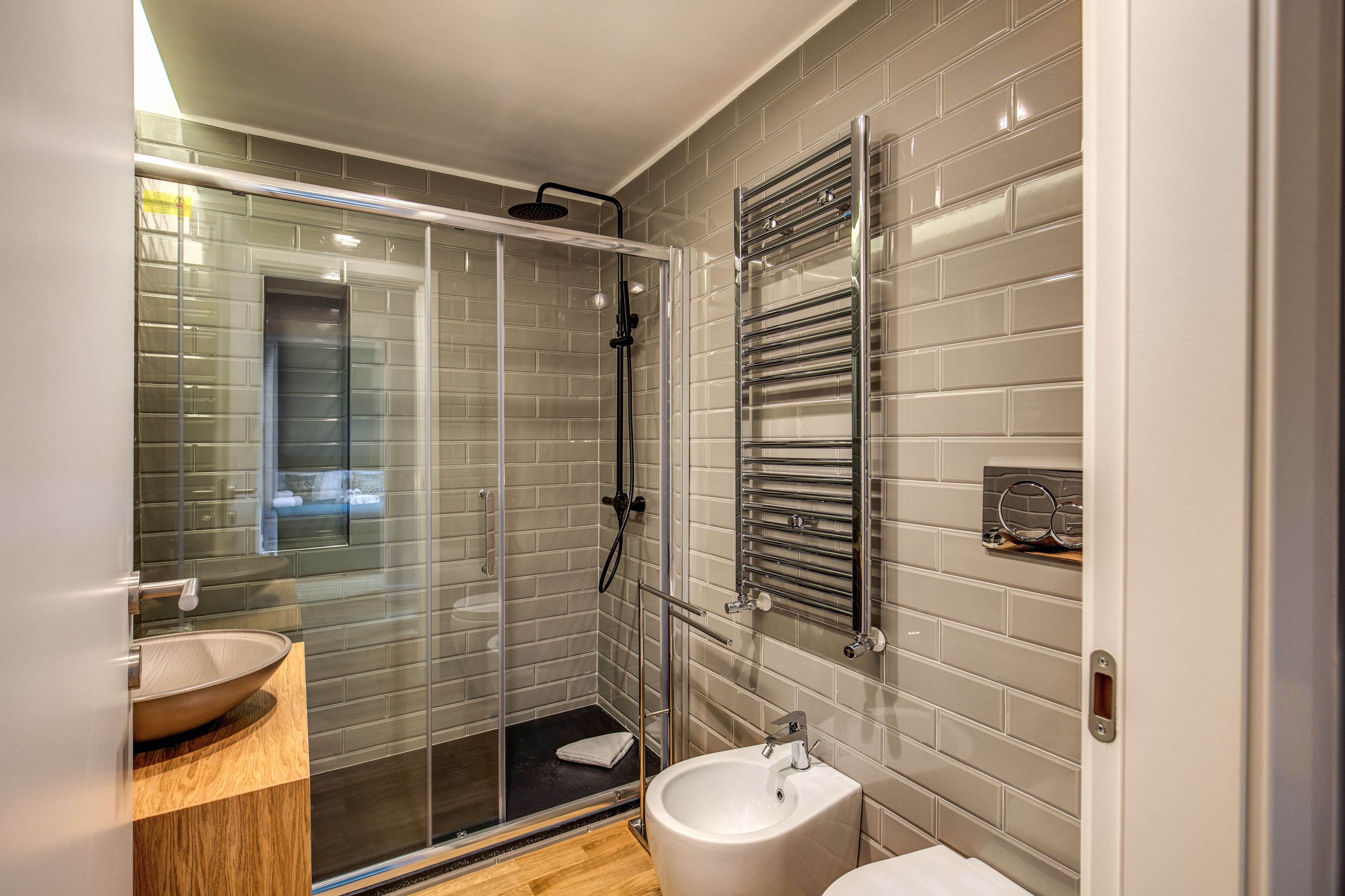 Een moderne badkamer met een douchecabine van glas, een witte wastafel en een handdoekrek.