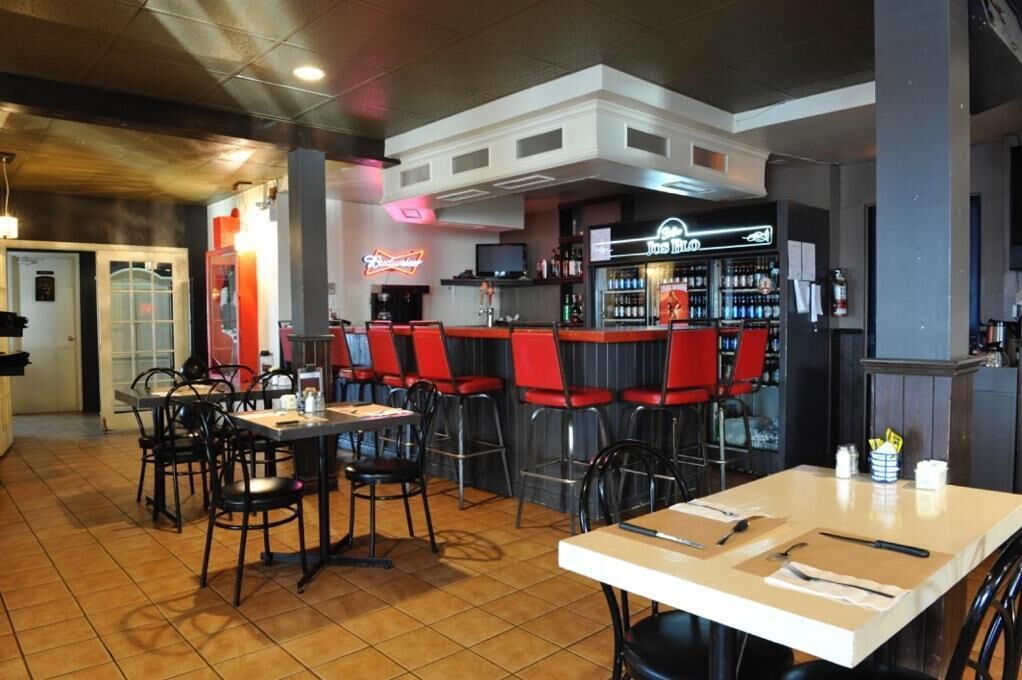 A restaurant with red bar stools, a bar area, and a seating area with tables and chairs.