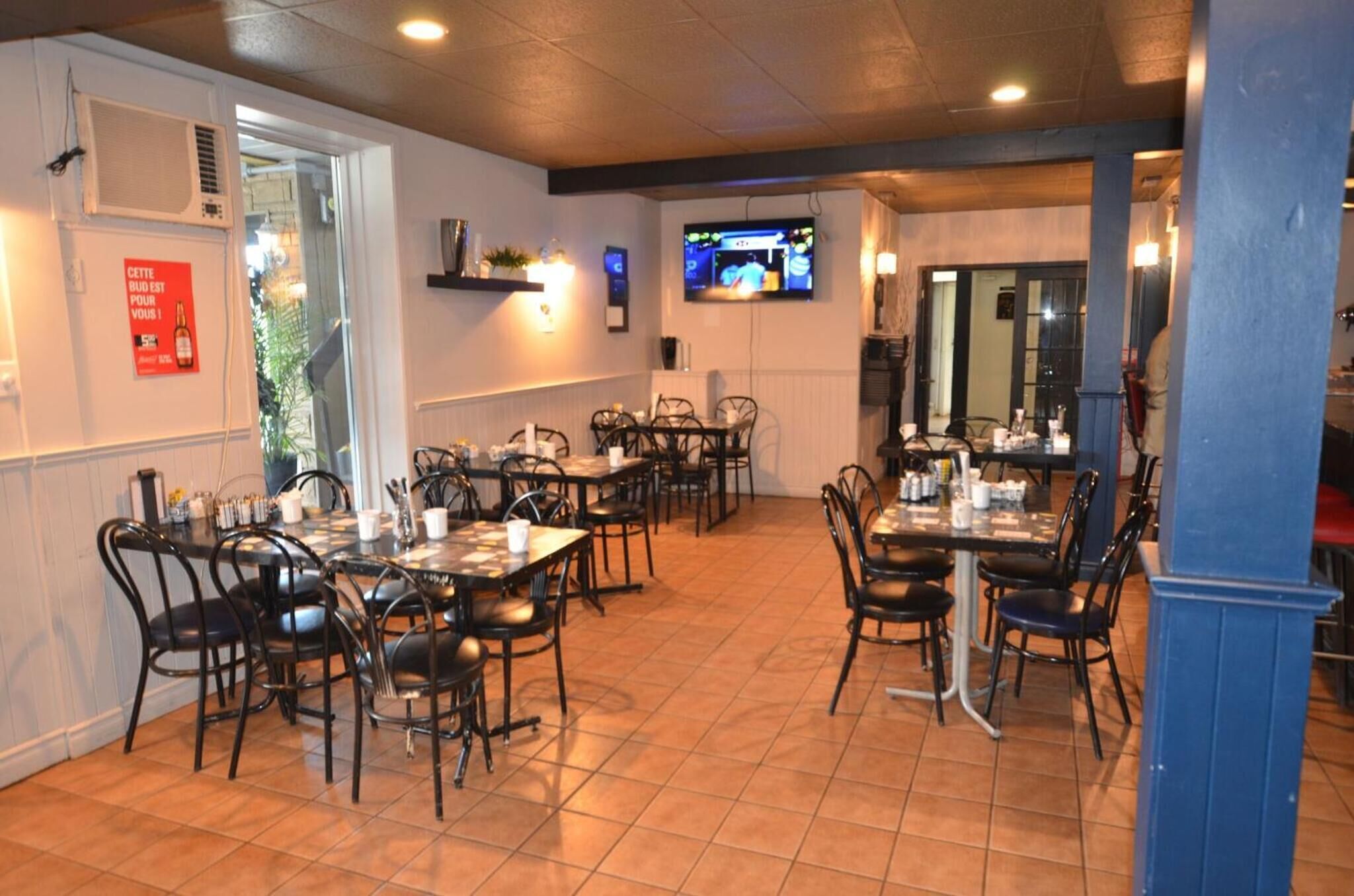 Un restaurante con varias mesas y sillas, un televisor montado en la pared y un letrero rojo en la pared.