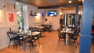 A restaurant with multiple tables and chairs, a television mounted on the wall, and a red sign on the wall.