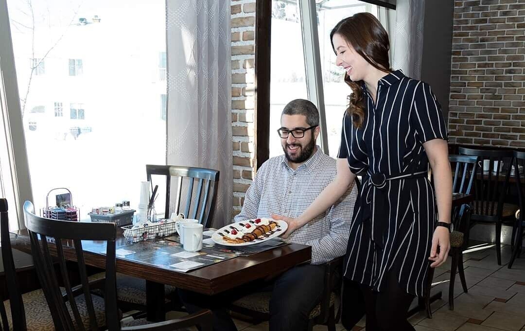 Un comedor con pared de ladrillo, ventanas amplias y una mesa con un plato de comida y una taza.