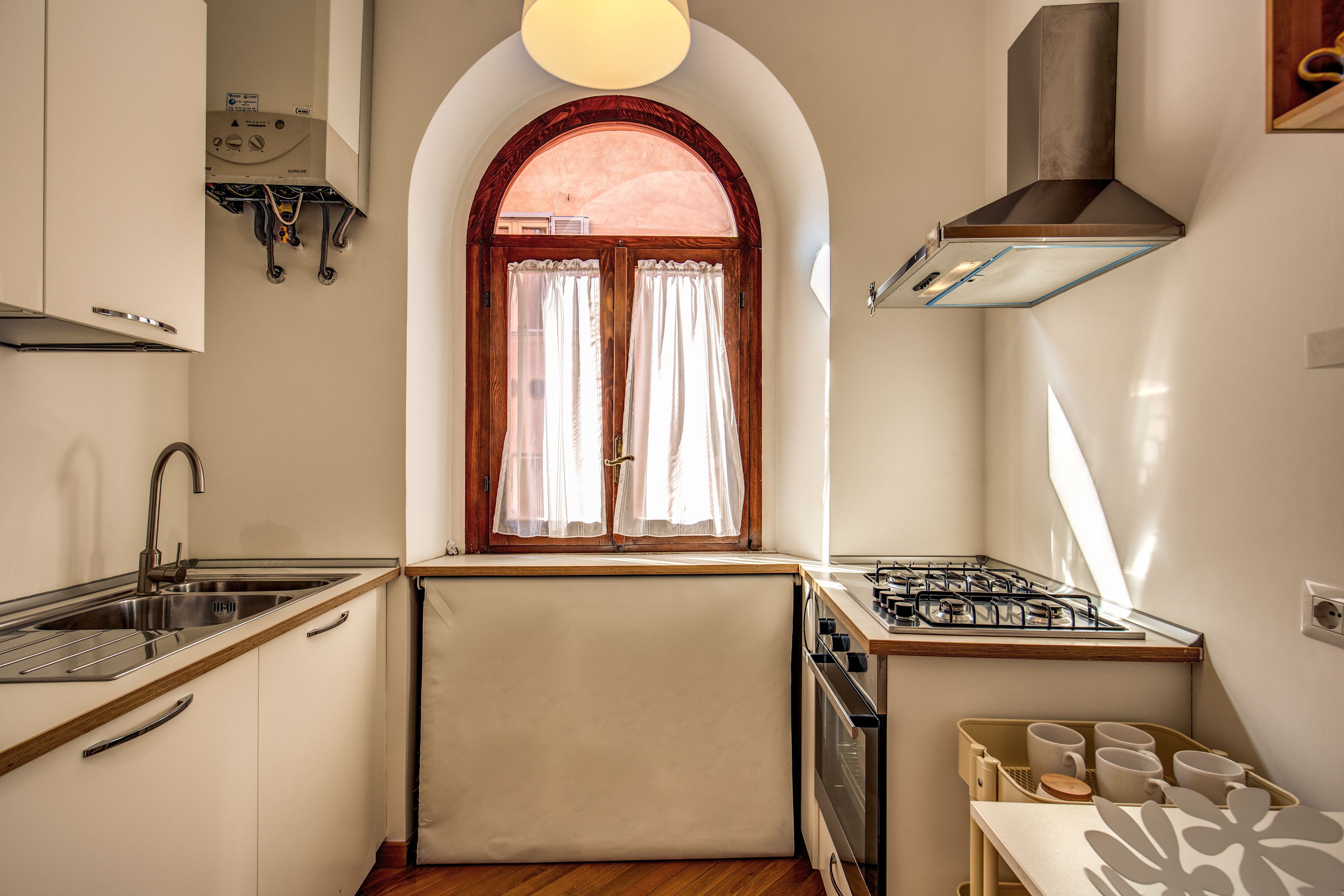 A compact kitchen with a gas stove, sink, and a window with curtains.