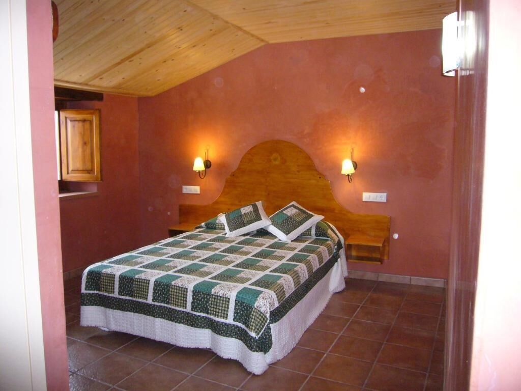 Une chambre à coucher avec une tête de lit en bois, deux lampes fixées au mur, une couvre-lit matelassé et une armoire en bois.