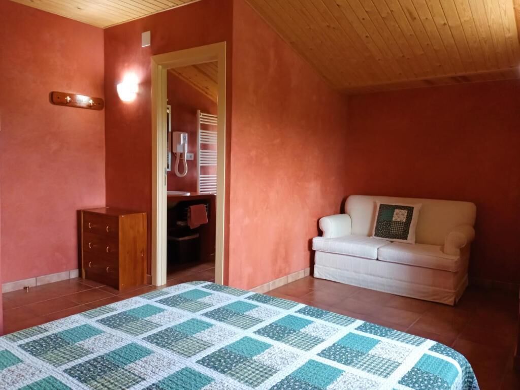 Quarto com teto de madeira, sofá branco, colcha acolchoada e cómoda de madeira.