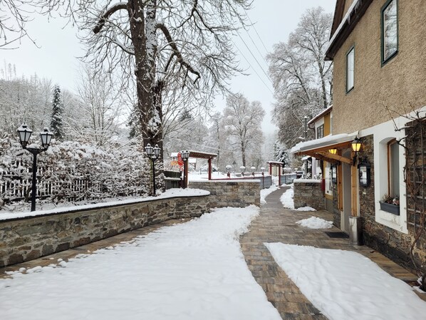 A snow-covered pathway leading to a building with stone walls and a wooden structure.