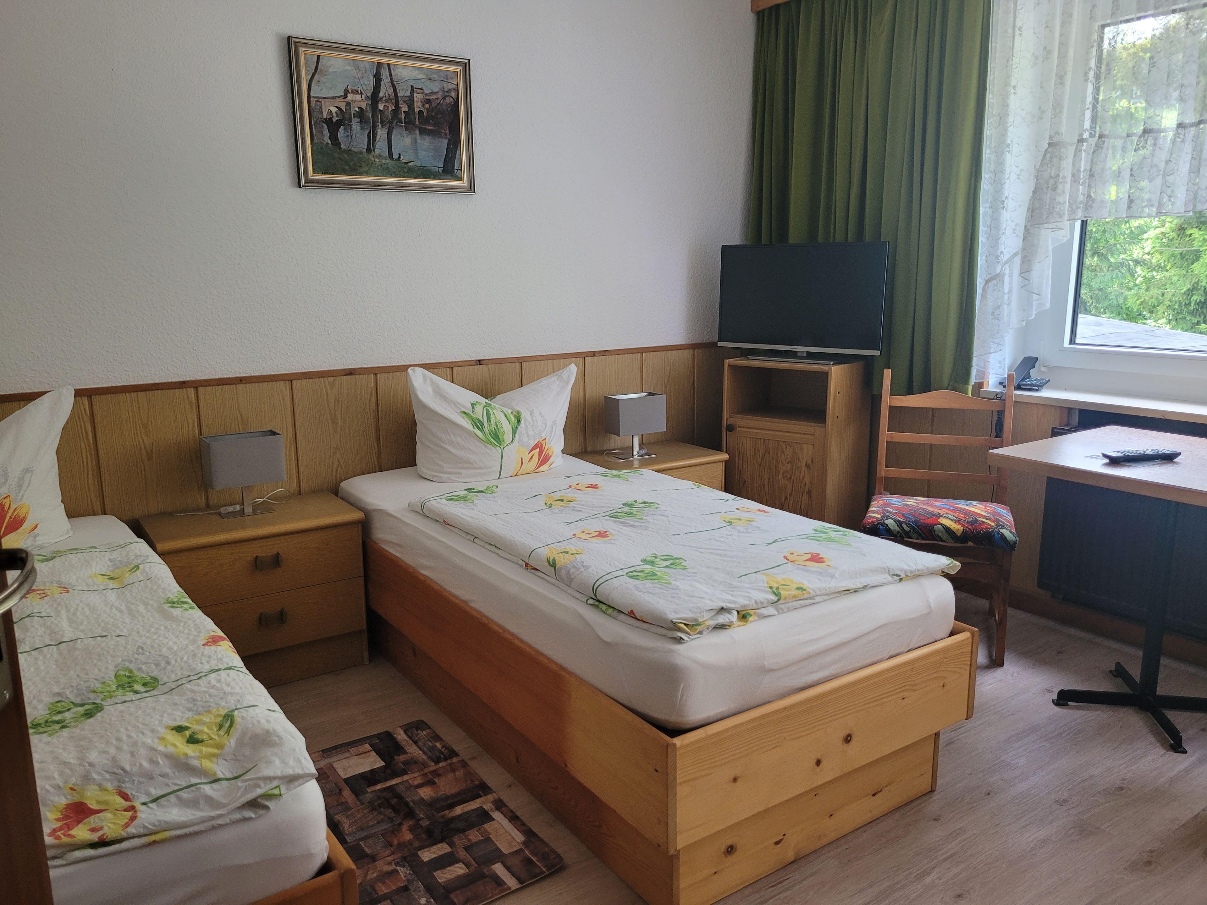 A bedroom with two single beds, a desk, a TV, and a window with curtains.