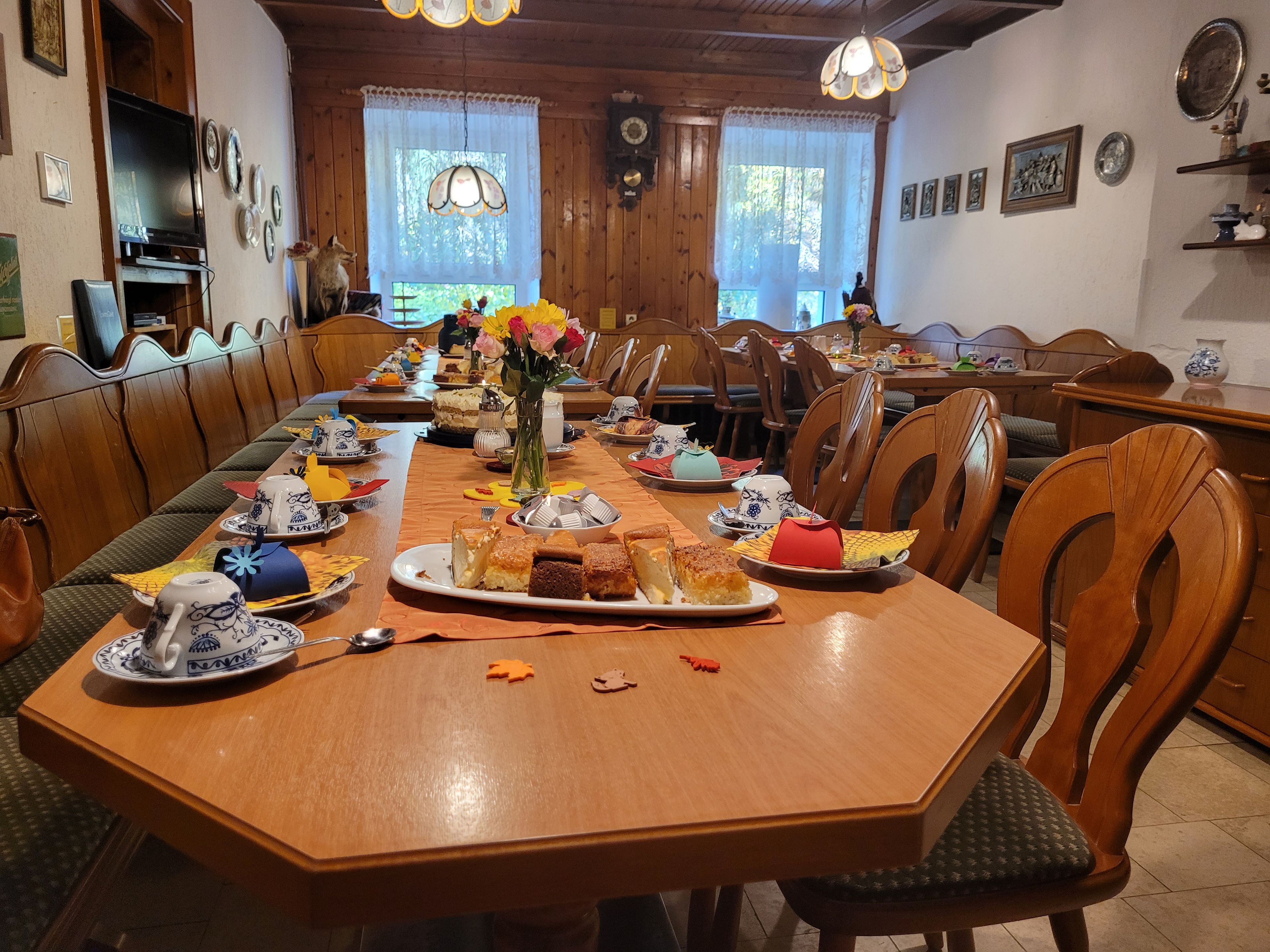 A long wooden dining table with chairs, a vase with flowers, and various dishes and utensils.