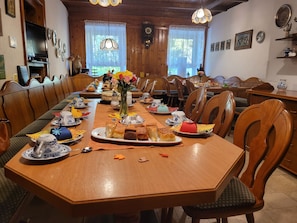 A long wooden dining table with chairs, a vase with flowers, and various dishes and utensils. - Landgasthof Fuchsbau (Eßbach)