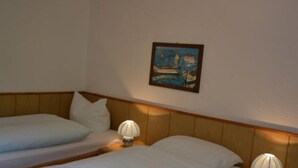 Een hotelkamer met twee enkele bedden, houten hoofdborden, wit beddengoed en een lijst met een schilderij van een boot aan de muur.