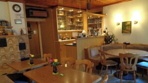 Een eetgedeelte met houten tafels en stoelen, een bar met flessenrekken, en een klok aan de muur.