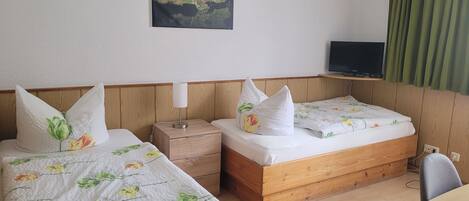 A hotel room with two beds, a wooden headboard, a bedside table with a lamp, a television on a stand, and a green curtain.