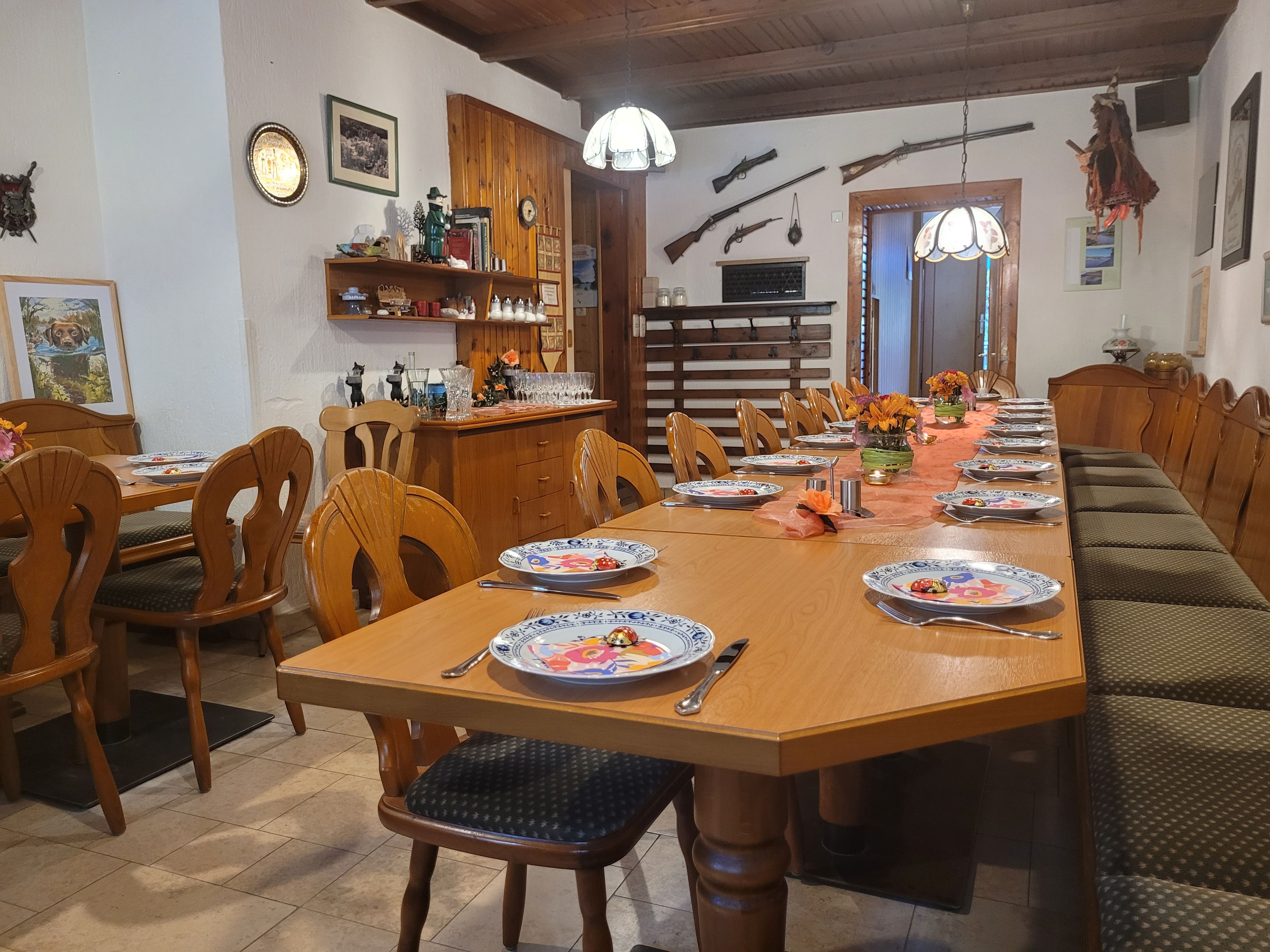 A dining area with a long wooden table, chairs, and benches. There are plates, cutlery, and glasses on the table.