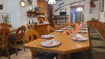 A dining area with a long wooden table, chairs, and benches. There are plates, cutlery, and glasses on the table.