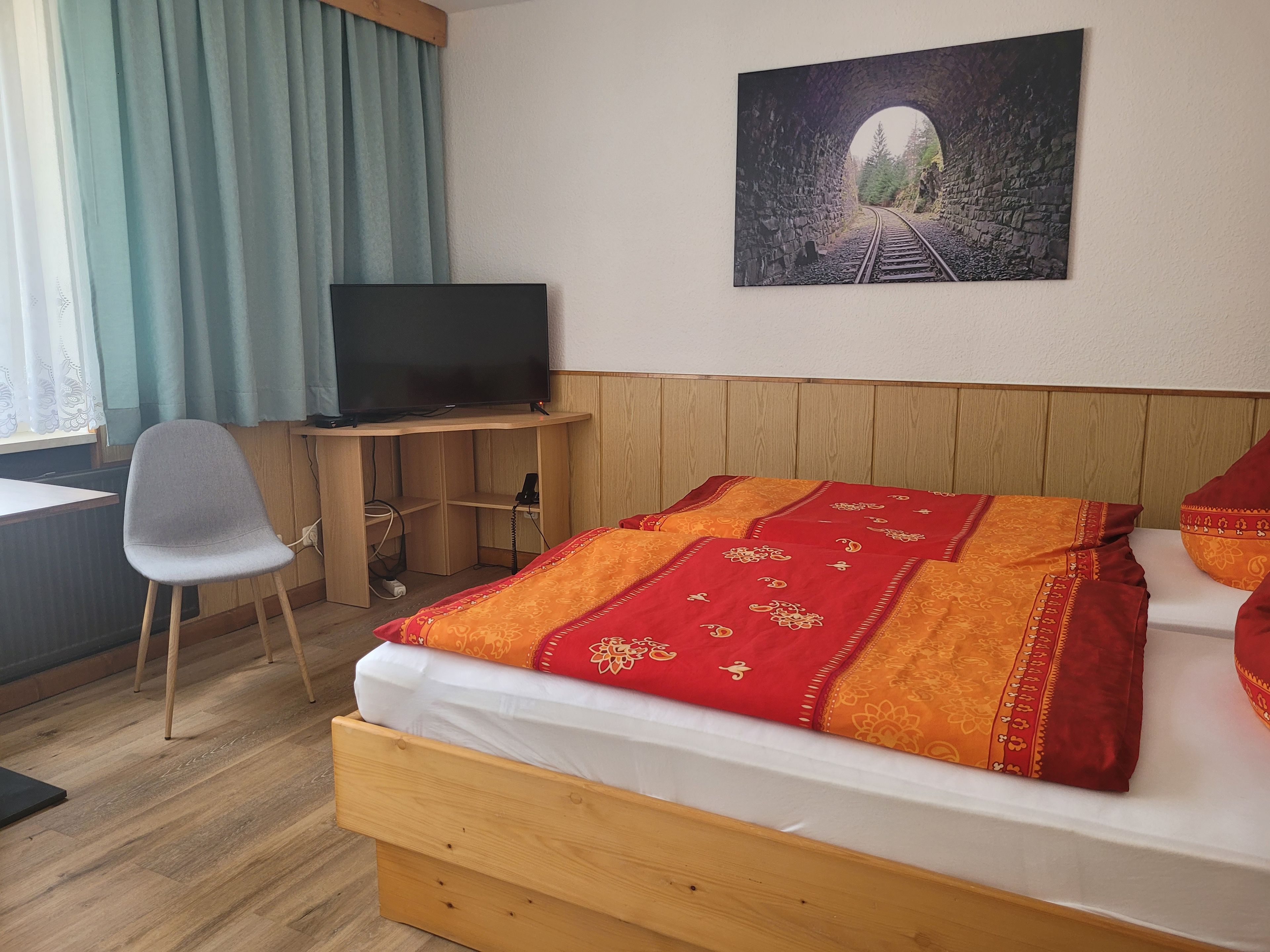 Habitación de hotel con una cama, un escritorio con televisor, una silla y un cuadro de un túnel en la pared.
