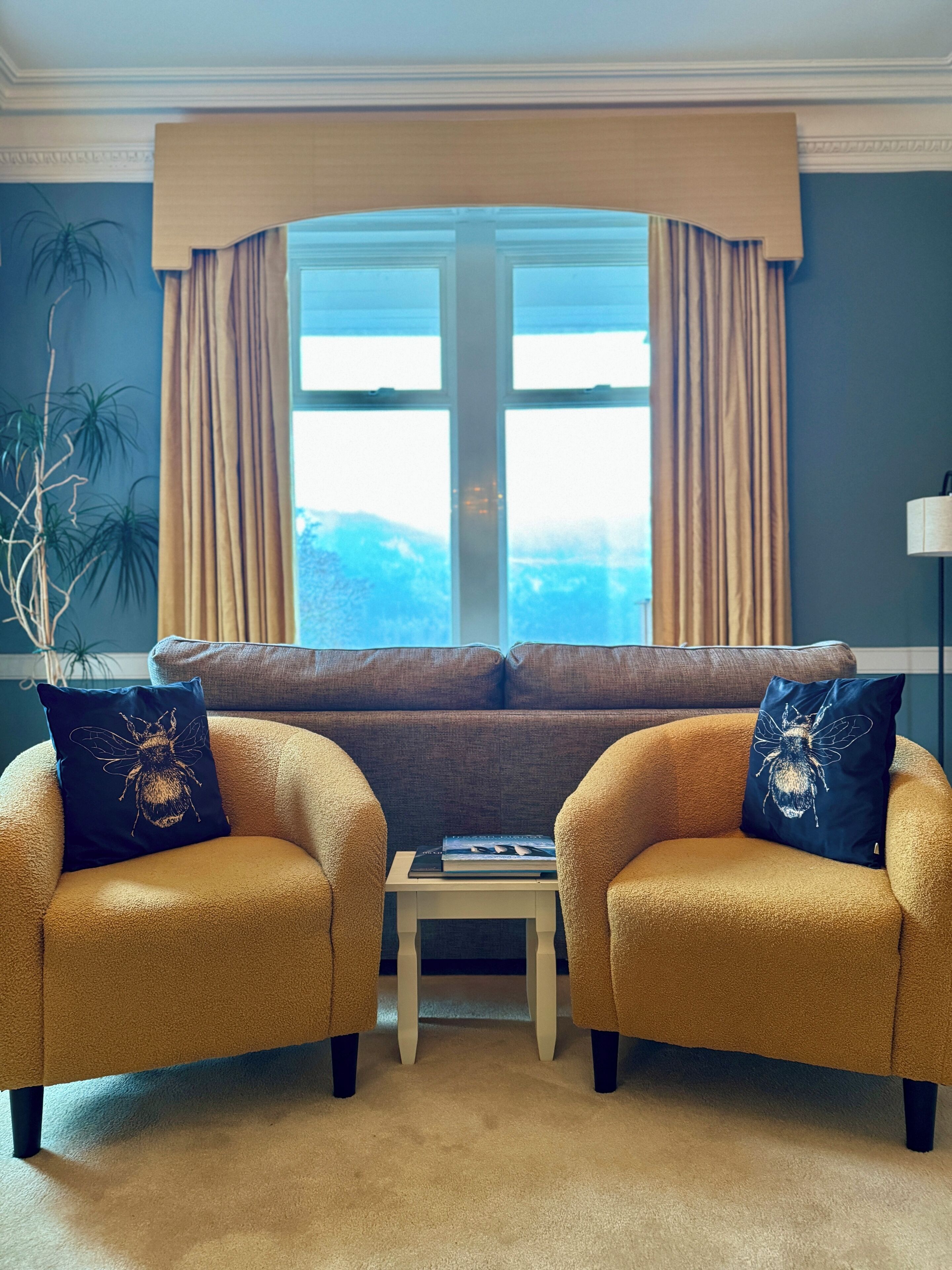 A living room with a beige sofa, two armchairs, a small table, and a window with curtains.