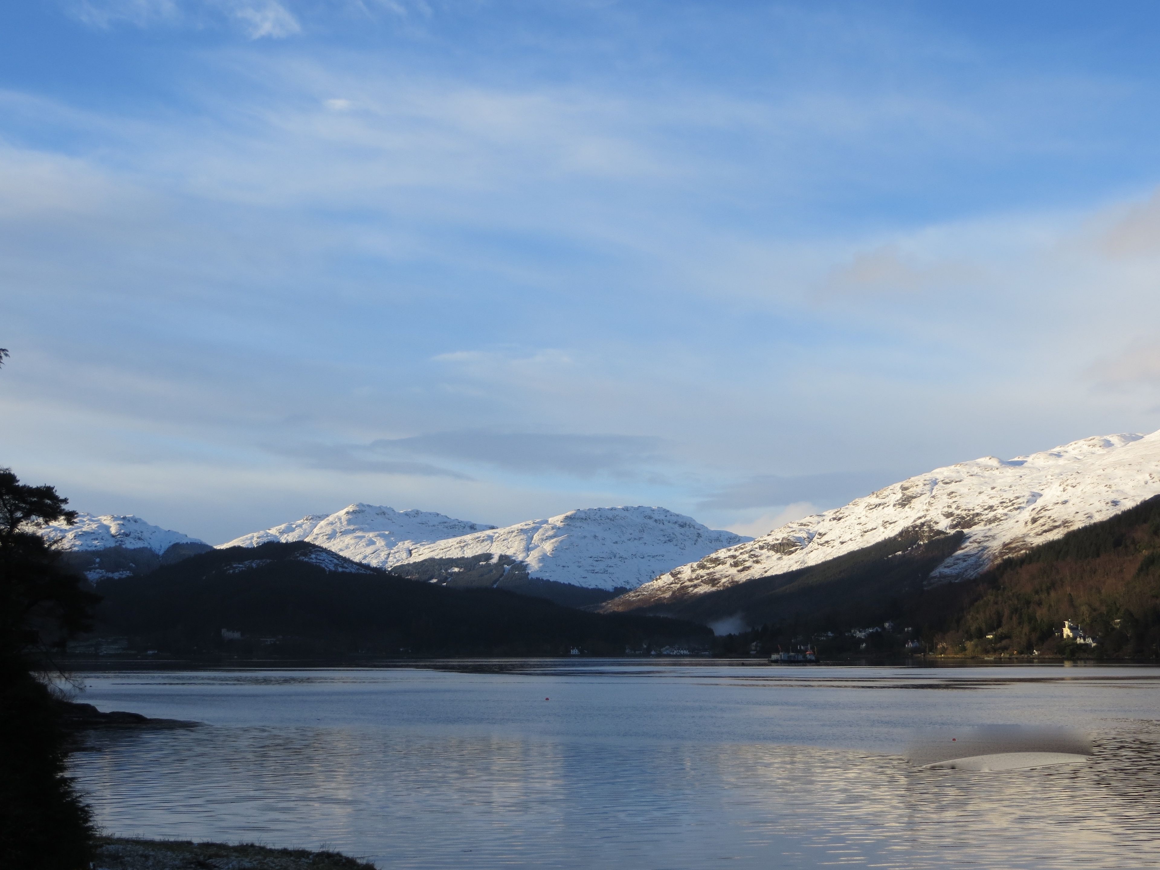 A calm lake with snow-capped mountains in the background and a clear sky.