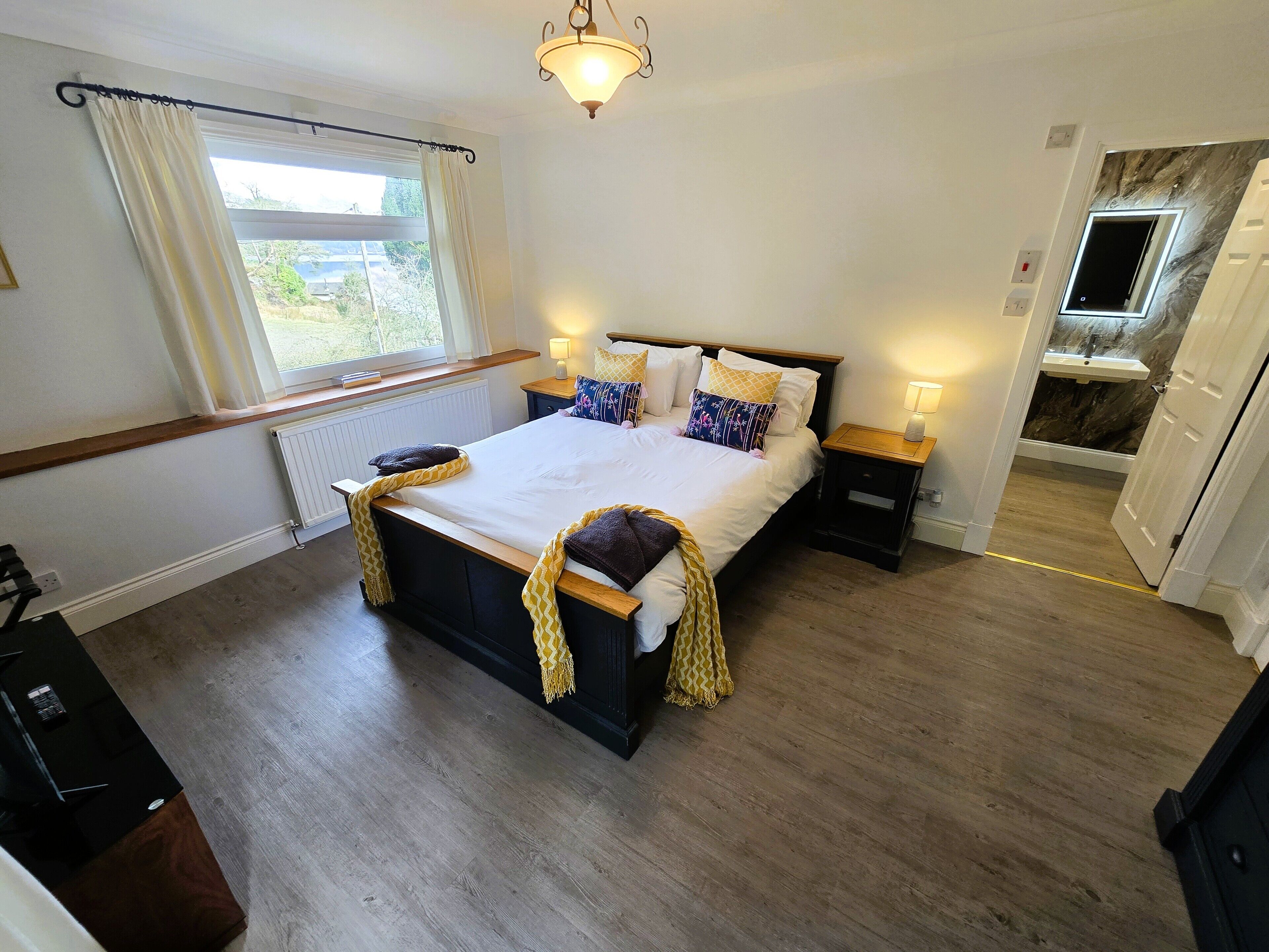 A bedroom with a large bed, bedside tables with lamps, a window with curtains, and a view of the outside.
